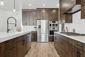 Kitchen with dark brown cabinets, appliances with stainless steel finishes, light wood-style floors, and recessed lighting