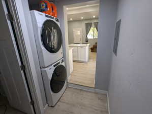 Laundry room with light wood-type flooring, stacked washing machine and dryer, and electric panel