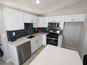 Kitchen with lofted ceiling, stainless steel appliances, backsplash, and white cabinets