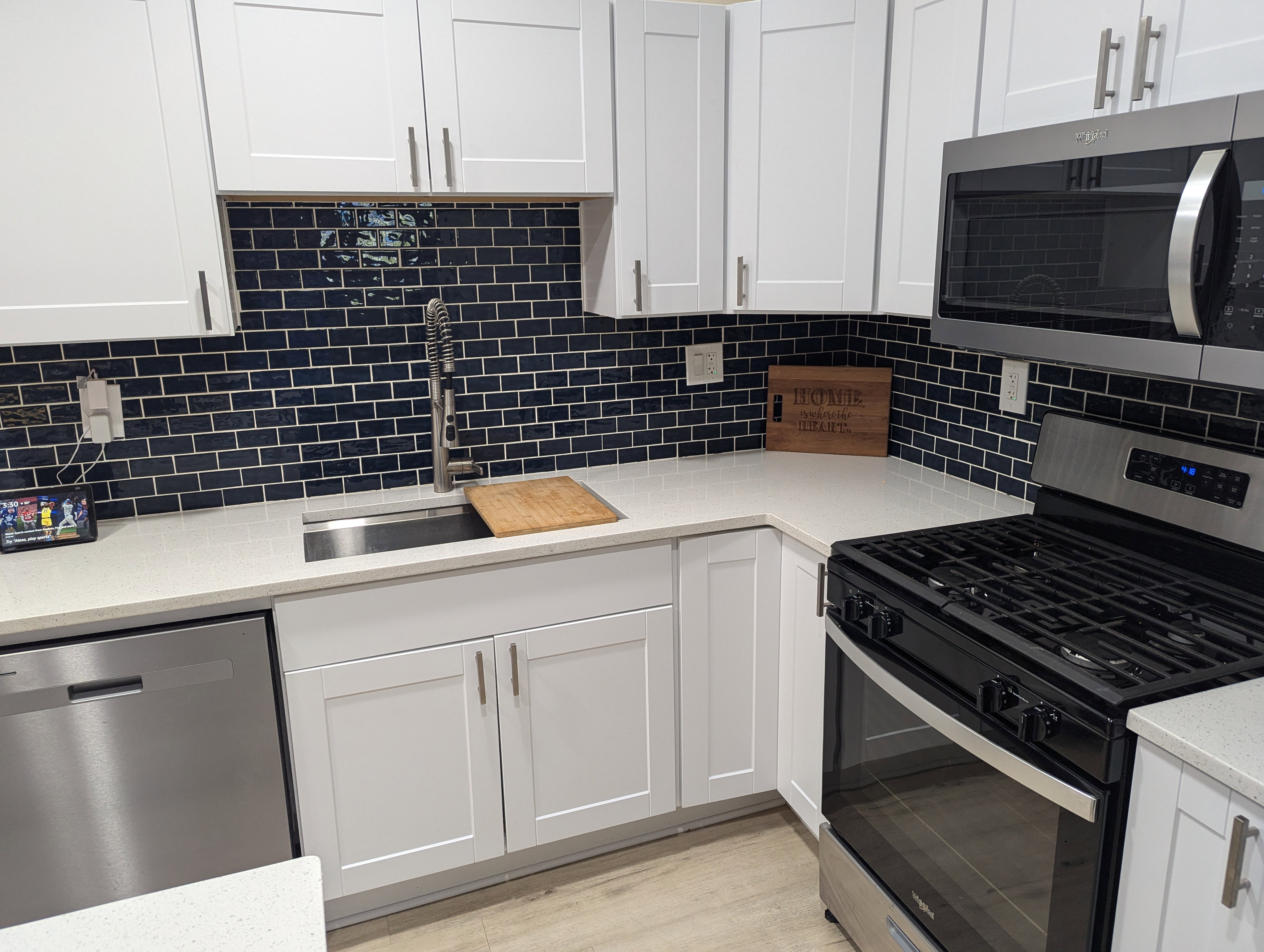 Kitchen with appliances with stainless steel finishes, light stone counters, backsplash, white cabinets, and light wood-style floors