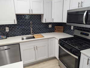 Kitchen with appliances with stainless steel finishes, light stone counters, backsplash, white cabinets, and light wood-style floors