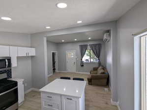 Kitchen with appliances with stainless steel finishes, recessed lighting, open floor plan, white cabinets, and light wood-style flooring