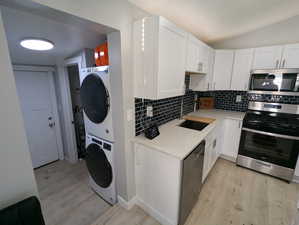 Kitchen featuring stainless steel appliances, light stone counters, light wood-style flooring, white cabinetry, and vaulted ceiling