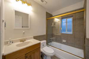 Full bathroom featuring bath / shower combo with glass door, vanity, a textured wall, and tile walls