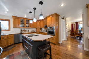 Kitchen with a breakfast bar, light countertops, dark wood-style floors, brown cabinets, and appliances with stainless steel finishes