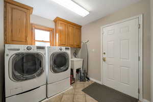 Laundry area with light tile patterned floors, cabinet space, and washer and dryer