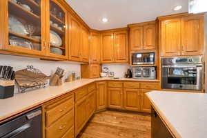 Kitchen featuring glass insert cabinets, light countertops, appliances with stainless steel finishes, brown cabinetry, and recessed lighting