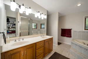 Full bath with light tile patterned floors, a shower stall, double vanity, a garden tub, and a walk in closet