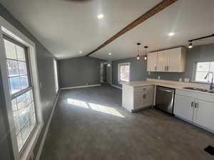 Kitchen with light countertops, white cabinetry, plenty of natural light, vaulted ceiling, and dishwasher