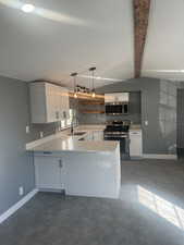 Kitchen featuring white cabinets, appliances with stainless steel finishes, pendant lighting, beamed ceiling, and light stone countertops