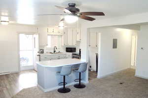 Kitchen with light countertops, ceiling fan, a kitchen breakfast bar, white cabinetry, and electric range