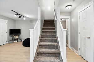 Stairway featuring rail lighting, wood finished floors, and a textured ceiling
