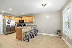 Kitchen featuring stainless steel appliances, light brown cabinets, a breakfast bar, light wood-style floors, and a peninsula