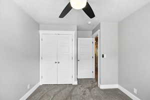 Unfurnished bedroom featuring dark carpet, a textured ceiling, a closet, and ceiling fan