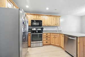 Kitchen with stainless steel appliances, light brown cabinets, light wood-style flooring, light stone countertops, and a peninsula