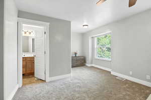 Unfurnished bedroom featuring light colored carpet, a ceiling fan, and ensuite bath