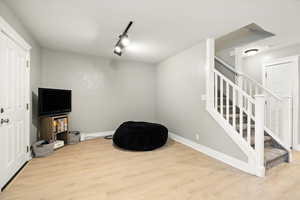 Sitting room with rail lighting, stairway, and light wood-style floors