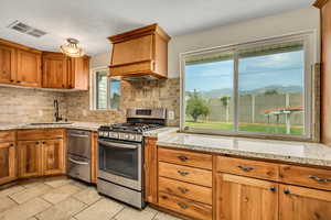 Kitchen with brown cabinets, appliances with stainless steel finishes, light stone countertops, tasteful backsplash, and light tile patterned floors