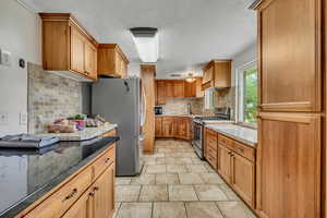Kitchen with backsplash, stainless steel appliances, brown cabinetry, dark stone counters, and a textured ceiling