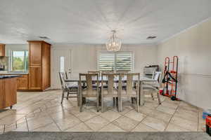 Dining room with light tile patterned floors, a textured ceiling, ornamental molding, and a chandelier