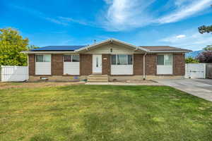 Single story home with brick siding, a gate, roof mounted solar panels, and entry steps