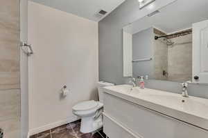 Full bath featuring double vanity, a tile shower, and dark tile patterned flooring