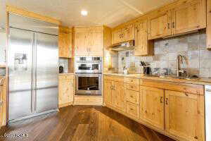 Kitchen with stainless steel appliances, light brown cabinetry, backsplash, and dark wood-type flooring