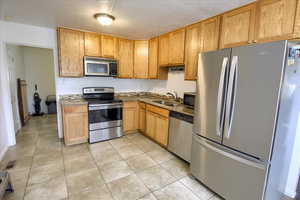 Kitchen with appliances with stainless steel finishes, light tile patterned floors, and a textured ceiling