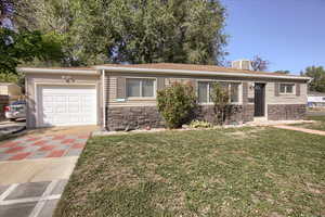 Single story home featuring stone siding, a front lawn, concrete driveway, and an attached garage