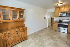 Kitchen with stainless steel appliances, light tile patterned floors, glass insert cabinets, and brown cabinets