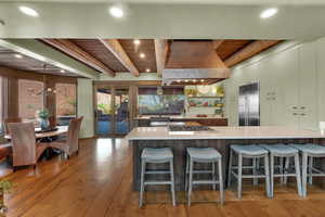 Kitchen with custom range hood, a wood ceiling with exposed beams, a breakfast bar area, open shelves, and appliances with stainless steel finishes