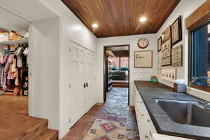 Laundry room with recessed lighting, tile counters, wooden ceiling, dark stone finish flooring, and white cabinets