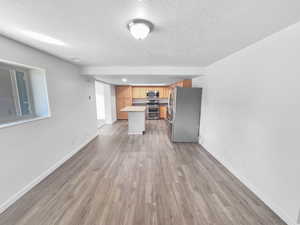 Kitchen with open floor plan, stainless steel appliances, light wood finished floors, a textured ceiling, and a center island