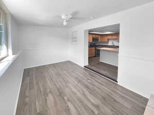 Unfurnished living room with dark wood-style flooring, a ceiling fan, and a wainscoted wall
