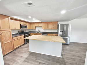Kitchen featuring stainless steel appliances, light wood-style floors, a textured ceiling, wood counters, and a center island
