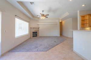 Unfurnished living room with a tray ceiling, a glass covered fireplace, ceiling fan, light tile patterned floors, and recessed lighting