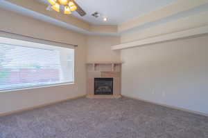 Unfurnished living room with a tiled fireplace, carpet, ceiling fan, a raised ceiling, and recessed lighting