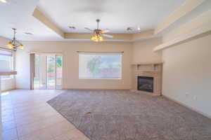 Unfurnished living room with a raised ceiling, a tile fireplace, light tile patterned floors, ceiling fan, and a chandelier