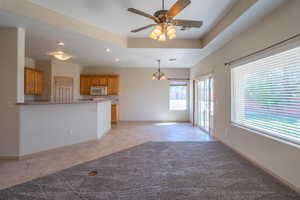 Unfurnished living room featuring light tile patterned floors, recessed lighting, a chandelier, a tray ceiling, and ceiling fan