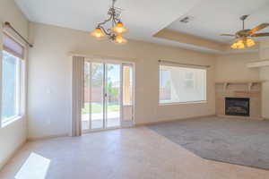 Unfurnished living room with a tray ceiling, a chandelier, light tile patterned floors, a high end fireplace, and a ceiling fan