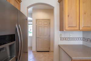Kitchen featuring stainless steel refrigerator with ice dispenser, backsplash, arched walkways, and light tile patterned floors