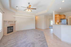 Unfurnished living room with a tray ceiling, a fireplace, ceiling fan, recessed lighting, and light tile patterned flooring