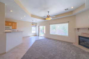 Unfurnished living room featuring a tray ceiling, recessed lighting, light tile patterned flooring, a premium fireplace, and ceiling fan