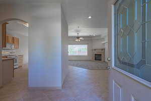 Foyer featuring light tile patterned flooring, a fireplace, ceiling fan, recessed lighting, and arched walkways