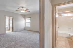 Unfurnished bedroom with connected bathroom, multiple windows, and ceiling fan