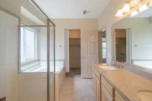 Full bath featuring a stall shower, a garden tub, double vanity, light tile patterned flooring, and a walk in closet