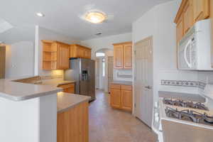 Kitchen featuring white appliances, arched walkways, open shelves, backsplash, and a peninsula