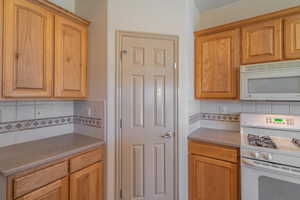 Kitchen with white appliances, tasteful backsplash, and light stone countertops