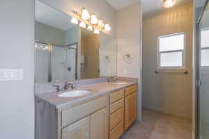 Bathroom with double vanity, light tile patterned flooring, and a shower stall