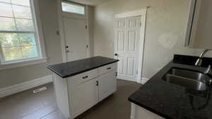 Kitchen featuring white cabinetry, dark stone countertops, a textured wall, a center island, and dark tile patterned flooring